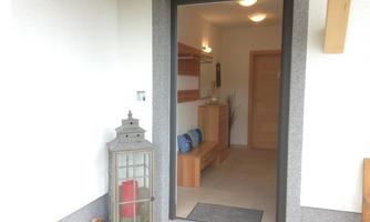 An inviting entrance area with a door and a beautiful lantern light. Inside, there are wooden shelves and a simple flooring.
