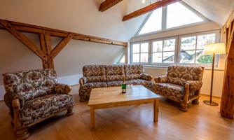 A cozy living room with two country-style sofas and a wooden table. Large windows let in plenty of light.