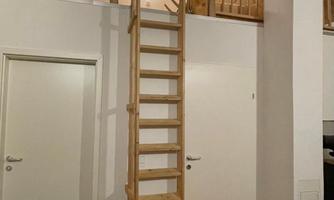 A living space with a wooden ceiling and stairs to an upper floor. To the right, there is a fire extinguisher on the wall.