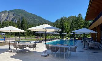 An inviting outdoor area with a pool and sun umbrellas. In the background, green mountains and trees can be seen.