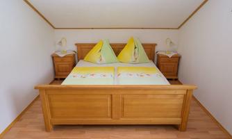 A cozy bedroom with a wooden bed and yellow cushions. Next to the bed are two nightstands.