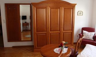 A cozy room with a large wooden cupboard and a round table. In the background, there is a mirror and a red armchair visible.