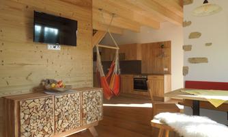 A modern wooden interior with a cozy dining area. In the background, there is a kitchen and a hanging swing.