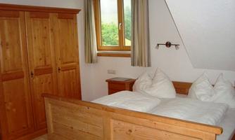 A cozy bedroom with wooden furniture. There is a double bed and a wardrobe next to a window.