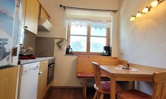 A bright kitchen with wooden details and a large window. There are chairs at the table, and the room feels cozy.