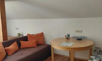 A cozy room with a couch and a round table. The wooden floors and light walls create an inviting atmosphere.