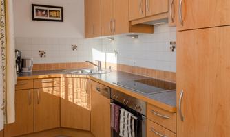 A modern kitchen with wooden cabinets and bright tiles. The kitchen is well-equipped and has plenty of daylight.