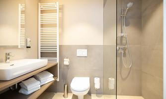 A modern bathroom with a shower, a sink, and a toilet. Towels are neatly stacked on a shelf.