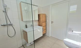 A modern bathroom with a glass shower and stylish wood and white furniture. The space is bright and cheerfully designed.