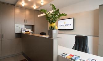 A modern reception area with an office. A plant is on the reception counter and a screen displays the logo "Vitus Steyr".