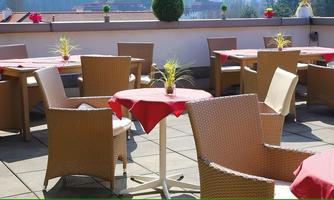 A cozy terrace with round tables and chairs. Small plants and red tablecloths are decorated on the tables.