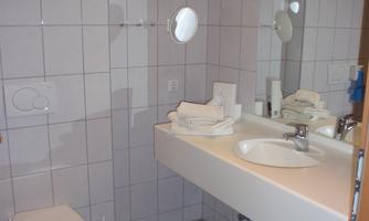 A modern bathroom with white tiles and a sink. In the room, there is a toilet and a mirror visible.