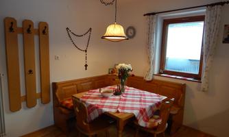 A cozy dining area with a wooden table and chairs. On the table lies a red and white tablecloth and a vase with flowers.
