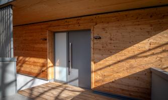 A modern wooden house with an elegant glass door. The walls are made of light wood and the light casts interesting shadows.