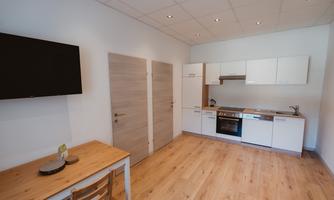 A bright, modern kitchen unit with a dining table and chairs. The room has a warm wooden floor and is well-lit.
