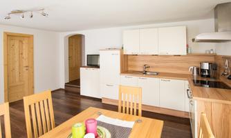 A modern kitchen with wooden shelves and white cabinets. Fresh fruits are on the table, and there is space for several people.