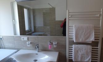 A modern bathroom with a sink and a large mirror. There is a towel warmer with clean towels.