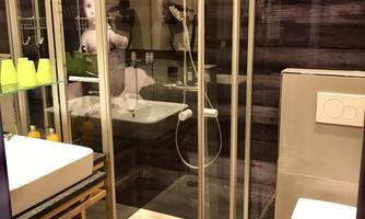 A modern bathroom with a glass shower and a white sink. The floor is tiled with wooden tiles and the walls are harmoniously designed.