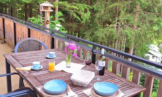 A beautiful table on a terrace overlooking trees. The table is set with plates, glasses, and a vase with flowers.