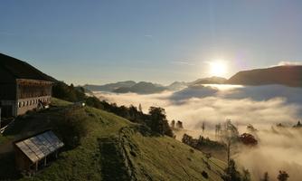 A picturesque landscape with gentle hills and a clear sky. The sun rises above the clouds, bathing the scene in warm light.