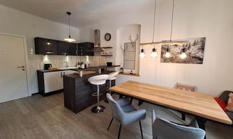 A modern kitchen with a light wood counter and elegant bar stools. The dining area features a large table and stylish chairs.