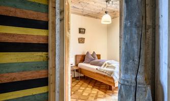 A cozy bedroom with a bed and decorative pillows. The walls are in soft colors and there is a warm wooden floor.