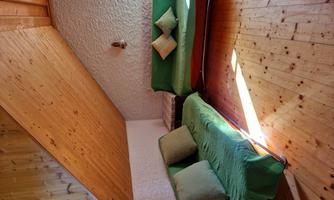 A cozy living room with two green sofas and cushions. The room has a wooden ceiling and a warm, inviting floor.
