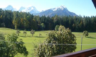 A picturesque landscape with green meadows and trees. In the background, snow-covered mountains can be seen.