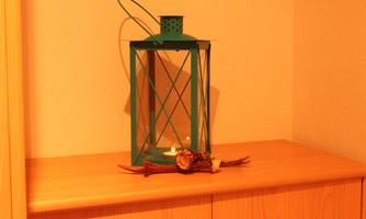 A green lantern stands on a wooden chest of drawers. Next to it lies a small decorative branch.