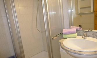 A small bathroom with a shower cabin and a sink. Colorful towels are neatly placed on the sink.