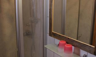 A small bathroom with a shower cubicle and a sink. The room is reflected in the mirror, and red towels are lying on the sink.