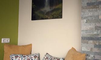 A cozy living area with a gray sofa and colorful cushions. A picture of a waterfall hangs on the wall.