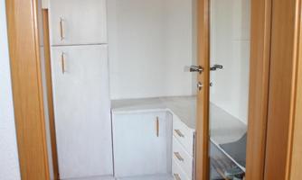 A bright hallway with a white cupboard and a small shelf. There's a carpet on the floor, and a toy is in the corner.
