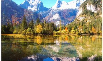 A picturesque mountain landscape with snow-covered peaks and colorful autumn forest. The clear lake perfectly reflects the surroundings.