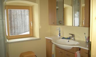 A modern bathroom with bright walls and wooden elements. A sink, mirror, and a window create a friendly atmosphere.