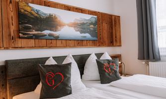 A cozy bedroom with two beds and decorative cushions. On the wall hangs a picture of a picturesque landscape with a tranquil lake.