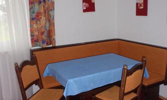 A cozy dining area with a corner bench and a table. The walls are decorated with colorful curtains and pictures.
