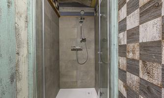 A modern shower with glass walls and a gray tiled wall. The floor is white and the surroundings have rustic wooden elements.