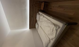 A simple bedroom with a double bed and a wooden chair. The walls are partially made of wood and there is soft, indirect lighting.