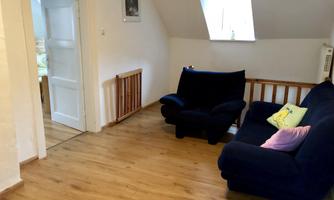 A cozy room with a blue sofa and warm wooden floor. There is an open door leading to another room.