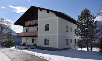 A modern house with two floors and a large balcony. It stands in a snow-covered landscape under a clear blue sky.