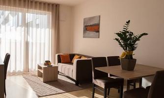 A bright living-dining room with a cozy sofa and a table. Plenty of daylight pours in through large windows.