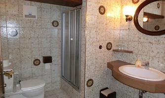 A simple bathroom with a shower, sink, and toilet. The walls are adorned with light tiles and decorative motifs.