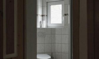 A bathroom with white tiles and a window. A toilet and a shower can be seen in the background.