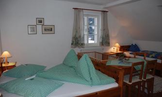 A cozy bedroom with wooden beds and checkered pillowcases. The room has a window with curtains and gentle lighting from bedside lamps.