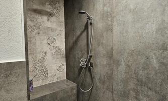 A modern shower with gray tiles and an elegant showerhead. The wall features a decorative pattern and provides a minimalist look.