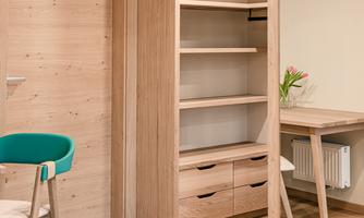 A modern room with wooden shelves and a large mirror. A desk and a chair are also available.