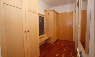 A bright hallway with wooden cabinets and a bench. The walls are painted in neutral colors.
