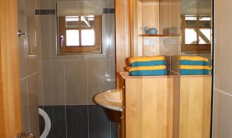A modern bathroom with wooden shelves and a sink. There are blue towels and tiled walls.