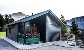 A charming wooden house in alpine style with a green flower box. Mountains are visible in the background.